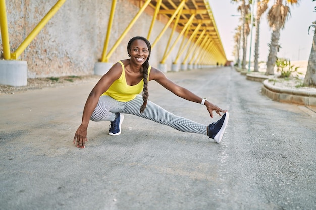 African american woman wearing sportswear stretching leg at street