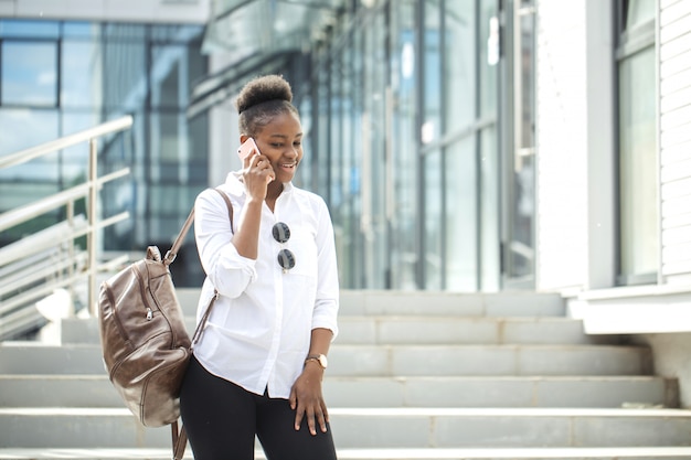 African american woman with backpack walking outdoor and talking on mobile phone