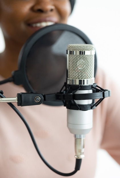 African american woman with headphones and a microphone recording a podcast in a recording studio