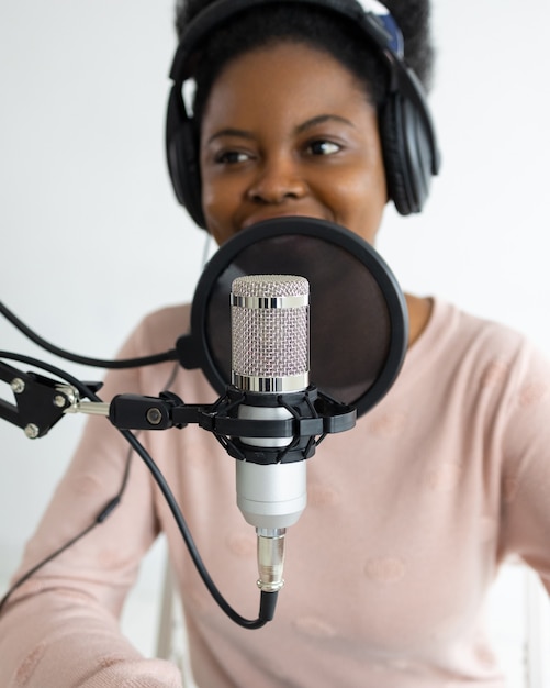 African american woman with headphones and a microphone recording a podcast in a recording studio