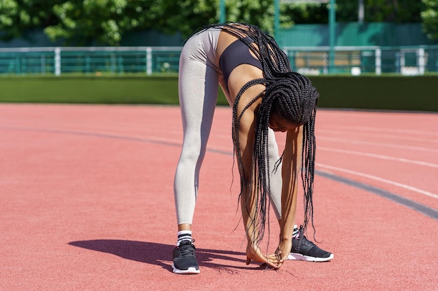 African American woman with long braids bends down doing effective exercise for stretching body