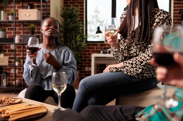 African american young adult woman laughing, smiling, guffawing, having fun at various ethnicities, nationalities friends social reunion, gathering, drinking wine, eating appetizers.