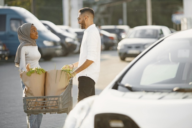 African Arabian couple stands with groceries near electric car. Charging electric car at the electric gas station