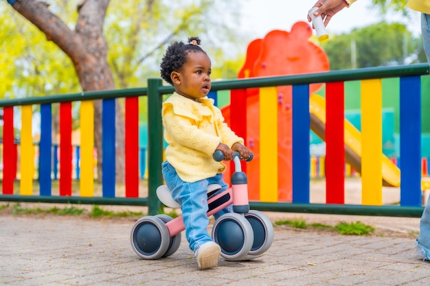 African baby girl riding a toy bike in a park