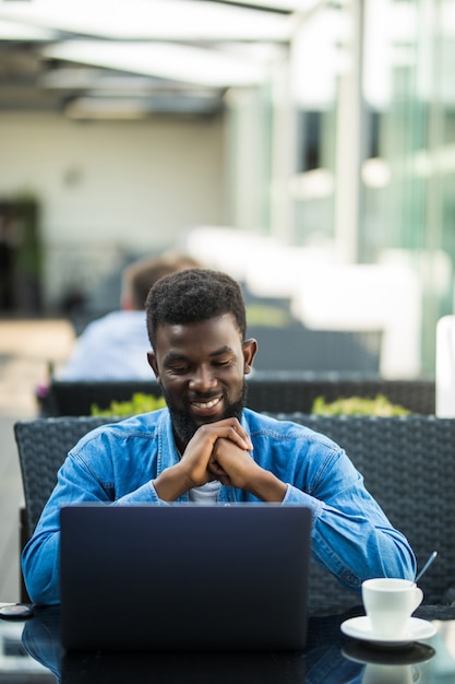 African business man sitting at table in cafe working with laptop and papers and drinking coffee