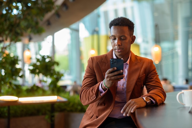 African businessman sitting in coffee shop using phone