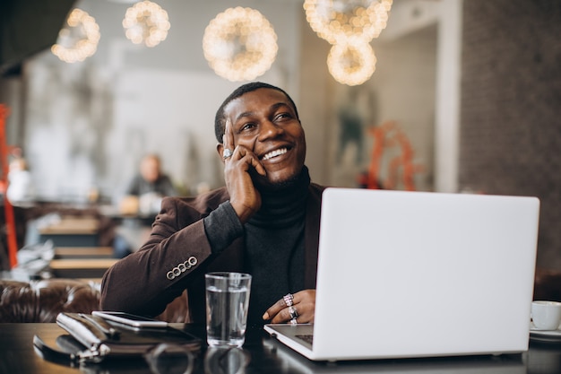 African businessman thinking and smiling while working on laptop in a restaurant.