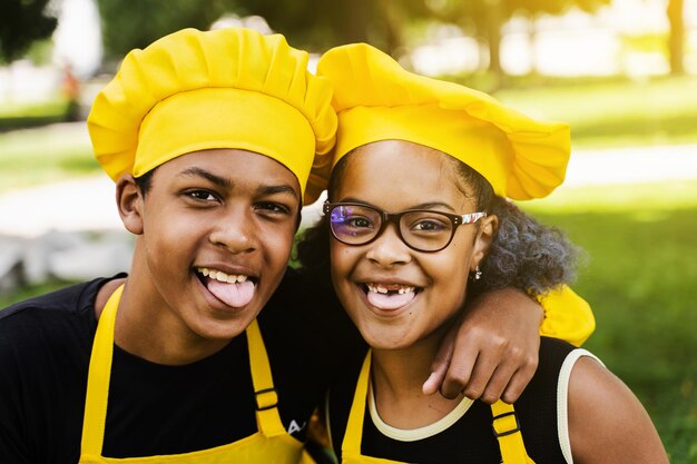 African children cooks in chefs hat and yellow uniforms grimacing and showing tongue each others African teenager and black girl have fun and cook food