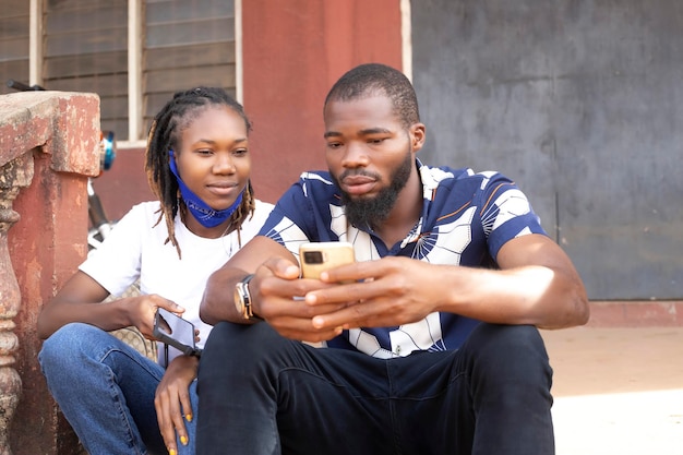 African couple using gadgets pretty girl with Afro typing a message on cell phone while her boyfriend sitting next to her looking down at the screen of her smart phone