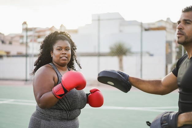 African curvy woman and personal trainer doing boxing workout session outdoor  Focus on girl face