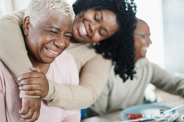 African daughter hugging her mum during lunch meal at home - Love and family concept - Main focus on senior woman face