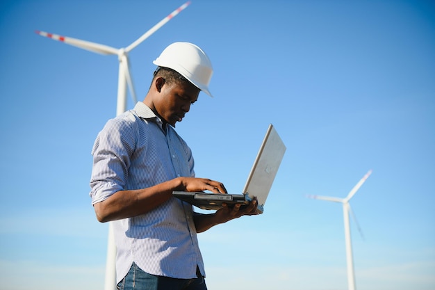 African Engineer standing and hoding laptop with wind turbine