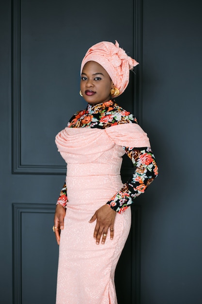 African female model in stylish pink dress, bright blouse and headscarf, posing at studio