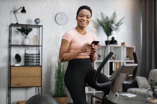 African female wearing sportswear writing message on her smartphone while working out