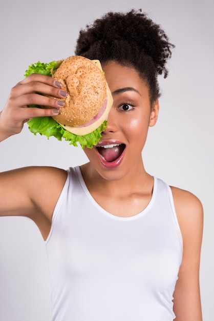 African girl closes her mouth and hides behind a hamburger.