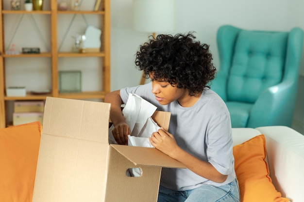 African girl unpacking delivery looking in box Happy woman opening carton box Female getting parcel looking at delivered goods items Satisfied client positive feedback quick express deliver