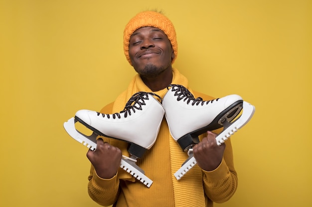 African guy in hat and scarf holds skates in his hands smiling at camera