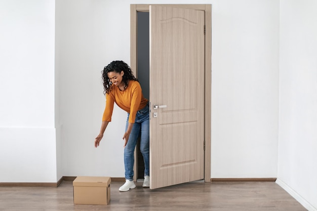 African Lady Receiving Box Standing Near Opened Door At Home