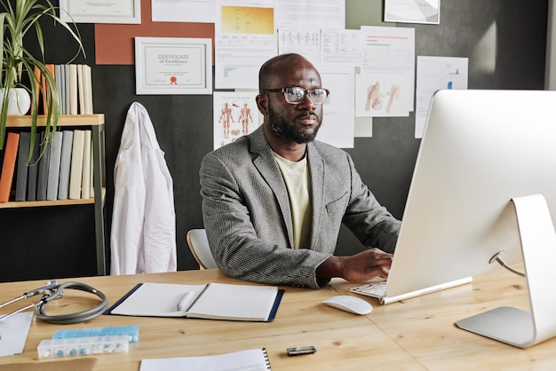 African male doctor sitting at his workplace at office and working on computer