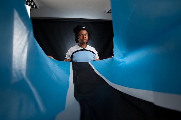 African man from Botswana with a flag smiling in a photo studio against a dark background