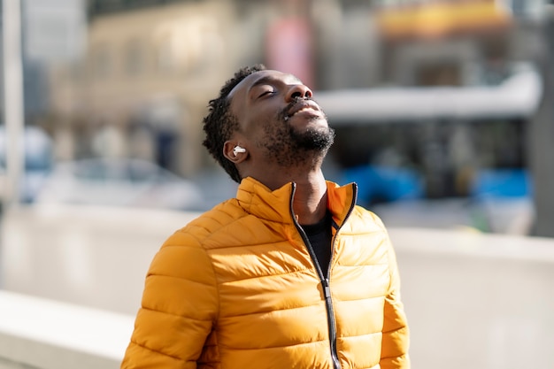 African man listening to music and breathing fresh air outdoors standing in the city