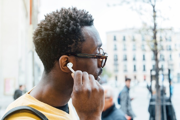 African man listening music through earphones. He's putting the earphone is his ear.