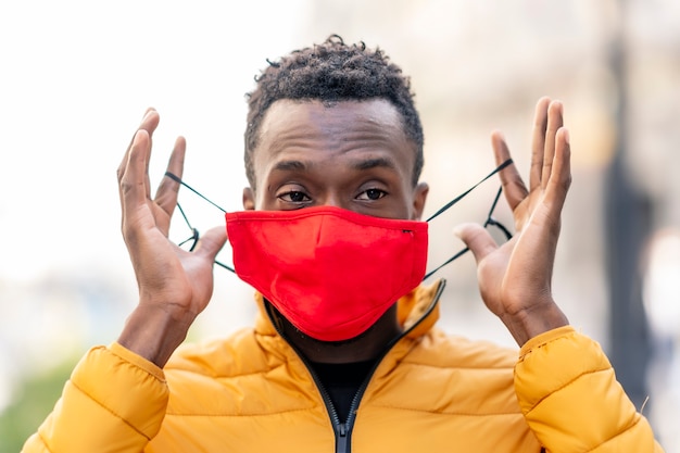 African man putting on a red face mask with unfocused city background