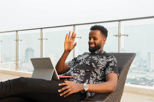 African man relaxing outdoors while using laptop computer and mobile phone