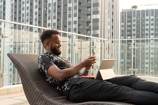 African man relaxing outdoors while using laptop computer and mobile phone