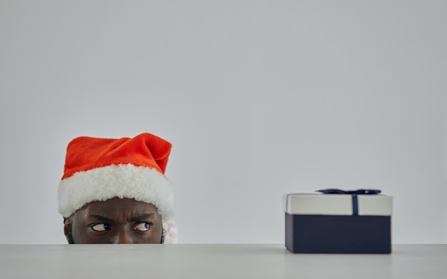 Photo the african man in the santa hat watching from the table with a gift