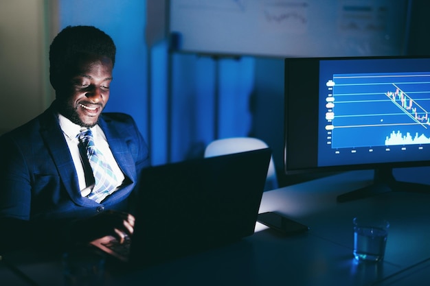 African man trader working at night time inside hedge fund office  Focus on face