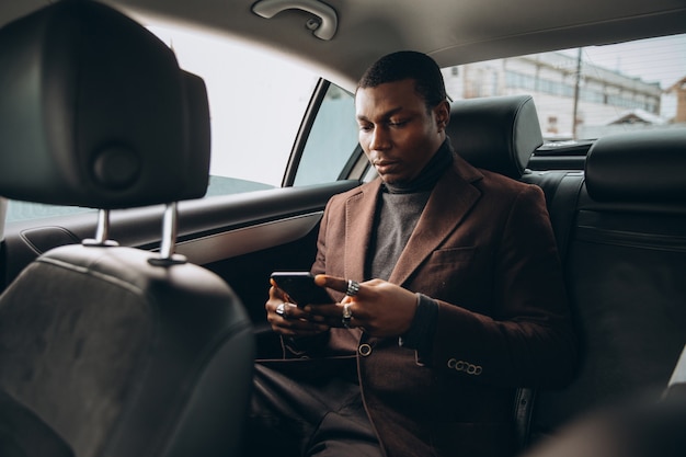 African man using smartphone while sitting on backseat in car. 