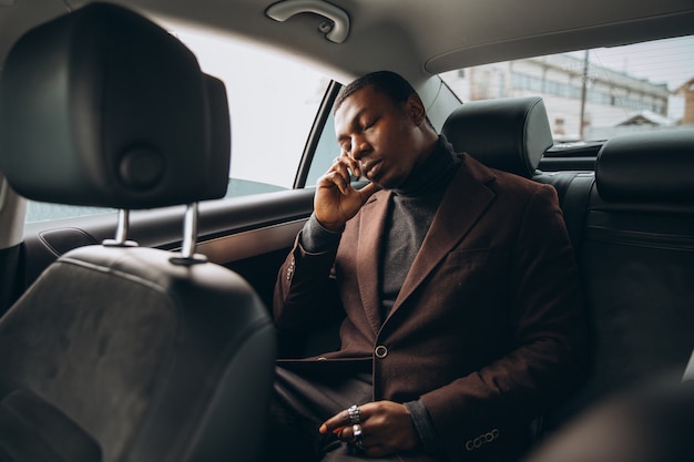 African man using smartphone while sitting on backseat in car. 