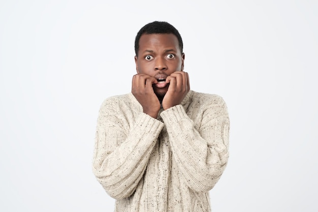 African man with nervous expression bites finger nails worries before interview