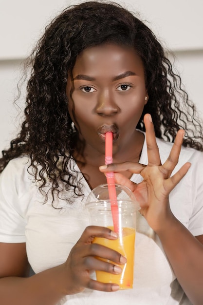 African model in white tshirt drinks an orange juice from a straw afro model girl has a glass of ora...