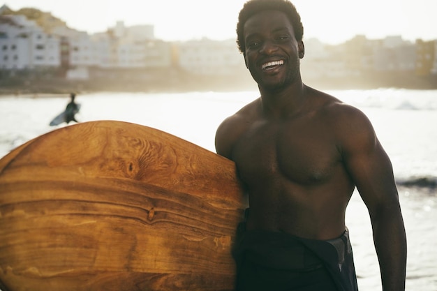 African surfer man holding vintage surf board on the beach at sunset  Focus on face