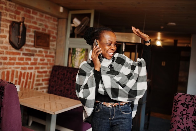 African woman in checkered cape posed at cafe and speak by mobile phone