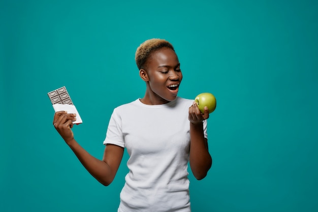 African woman holding apple and dark chocolate bar.