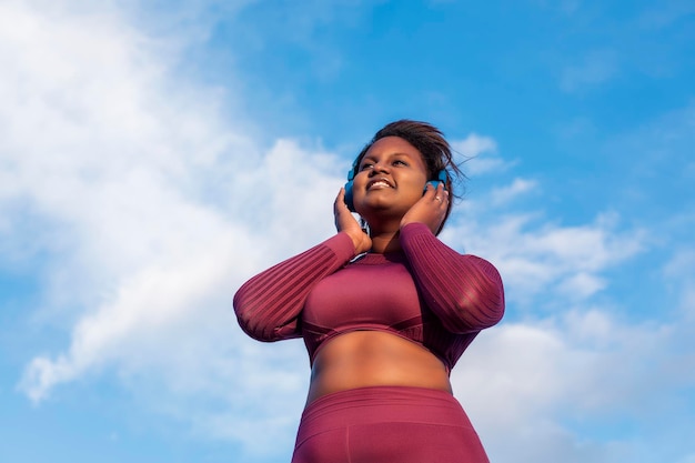 African woman listening to music through headphones with blue sky in the background