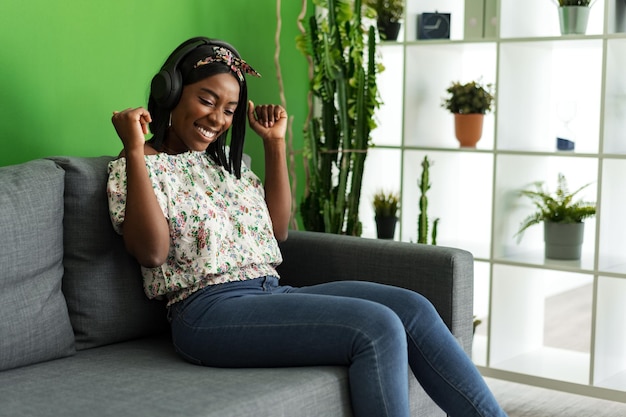 African woman listening to music with headphones while sitting on couch at home