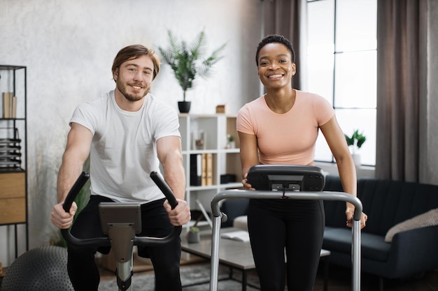 African woman running on treadmill and caucasian man training on exercise bike