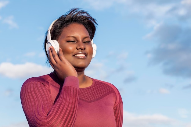 African woman sitting listening to music through headphones with the blue sky in the background