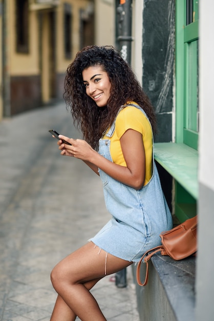 African woman sitting outdoors texting with her smart phone