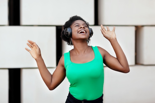 African woman smiles, listens to music with headphones and dances in the street.