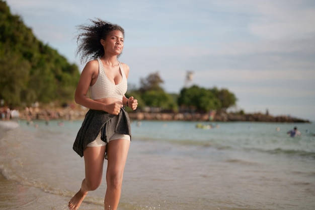 African woman in sport bra is running on beach for outdoor workout Portrait sexy Asian African lady preparing herself for fitness at beach