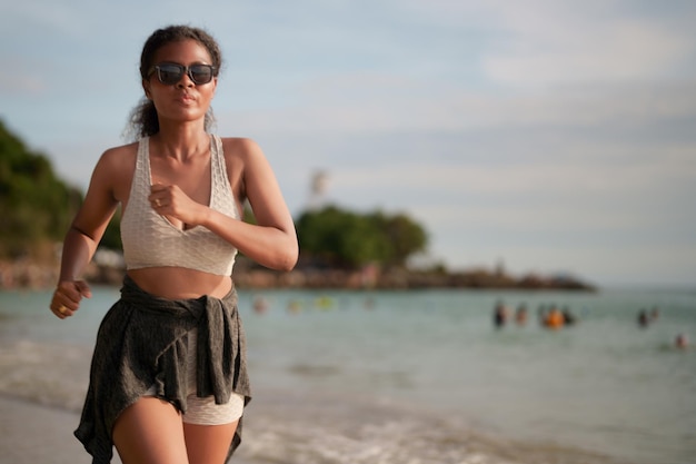 African woman in sport bra is running on beach for outdoor workout Portrait sexy Asian African lady preparing herself for fitness at beach