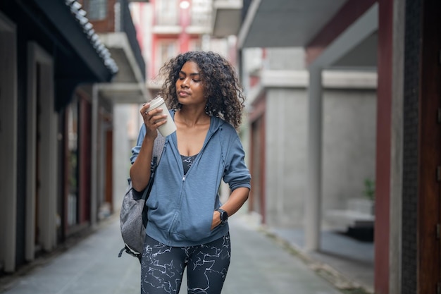 African woman sport healthy fit and firm slim drink water from cup on the hand fitness girl wearing sportswear and jacket walking at city and town Fitness and sport motivation