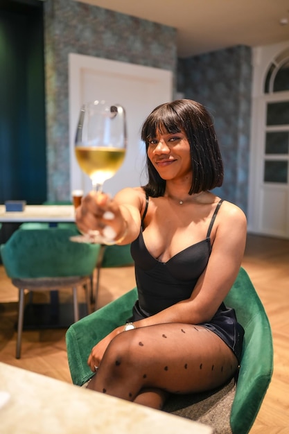 African woman toasting at camera sitting in a luxury bar