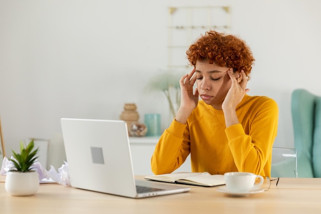 African woman touching temples experiencing stress Girl at home office tired of working feeling headache sick rubbing temples forehead Long laptop usage computer vision syndrome Office syndrome