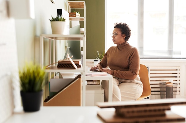 African young businesswoman sitting at her workplace in front of monitor and working on computer at